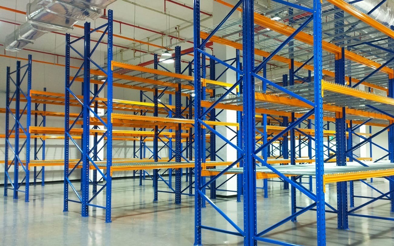 Tall heavy duty pallet racking with blue uprights, orange beams and wire mesh decking