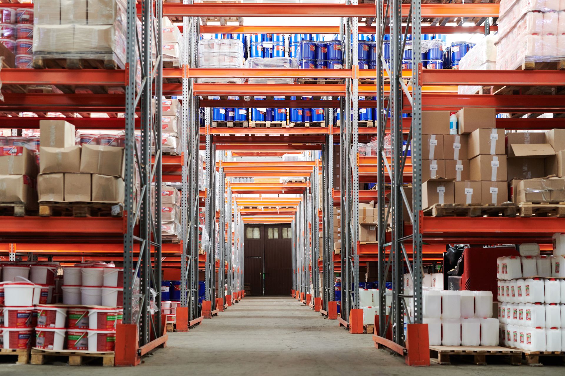 Warehouse aisle lined with pallet racking loaded with boxes and drums
